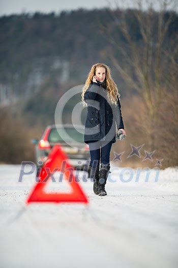 Young woman setting up a warning triangle and calling for assistance after her car broke down in the middle of nowhere on a freezing winter day Young woman setting up a warning triangle and calling for assistance after her car broke down in the middle of nowhere on a freezing winter day