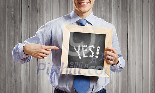 Young smiling businessman holding chalkboard with yes word
