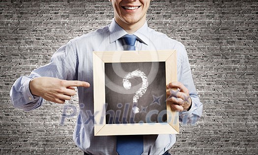 Young smiling businessman holding chalkboard with question sign Young smiling businessman holding chalkboard with question sign