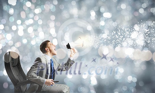 Young angry businessman sitting on chair and screaming in megaphone Young angry businessman sitting on chair and screaming in megaphone