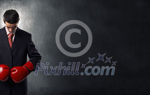 Young businessman in red boxing gloves on dark background Young businessman in red boxing gloves on dark background