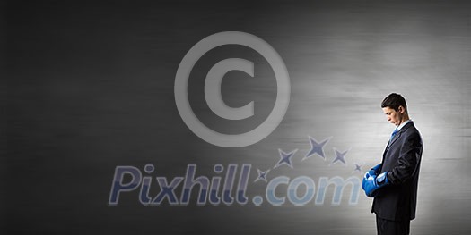 Young businessman in blue boxing gloves on dark background Young businessman in blue boxing gloves on dark background