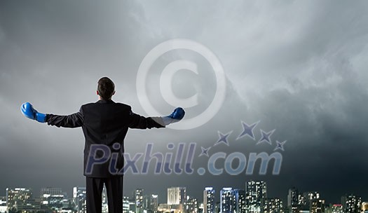 Back view of businessman in blue boxing gloves on city background Back view of businessman in blue boxing gloves on city background