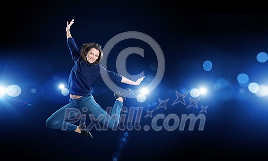 Young woman dancer jumping in spotlights on dark background