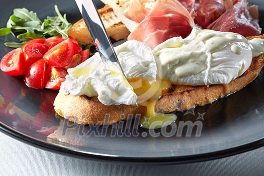 The knife cuts the Eggs Benedict on toasted bread with ham, tomatoes and sauce The knife cuts the Eggs Benedict on toasted bread with ham, tomatoes and sauce