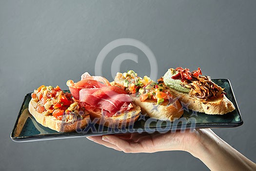 delicious variety of Italian bruschetta on a ceramic tray holds the hand of man delicious variety of Italian bruschetta on a ceramic tray holds the hand of man