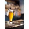 Glass of light beer served on wooden desk. Bar on background