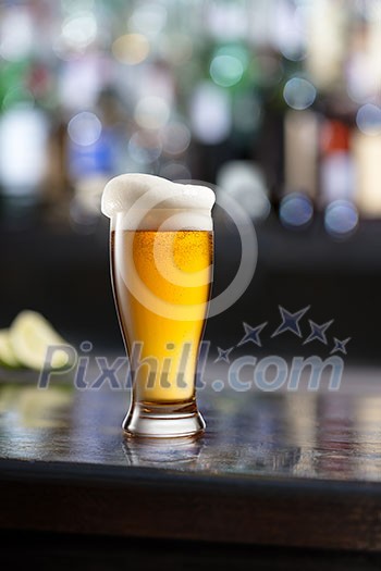 glass of beer with foam on black wooden a table in a bar on blurred bar background