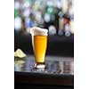 glass of beer with foam on black wooden a table in a bar on blurred bar background