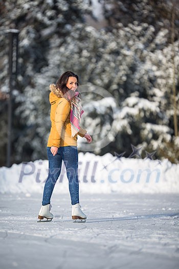 Young woman ice skating outdoors on a pond on a freezing winter day (color toned image; motion blurred image)