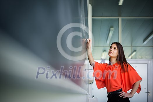 Pretty, young college student writing on the chalkboard/blackboard during a math class Pretty, young college student writing on the chalkboard/blackboard during a math class