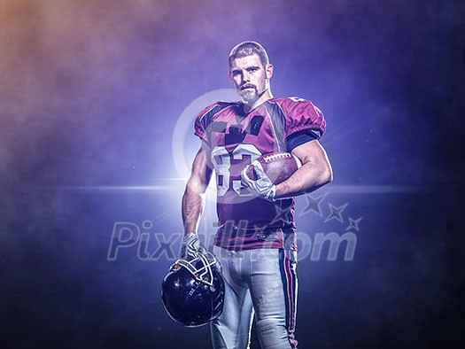 portrait of confident American football players holding ball while standing on the big modern stadium field with lights and flares at night