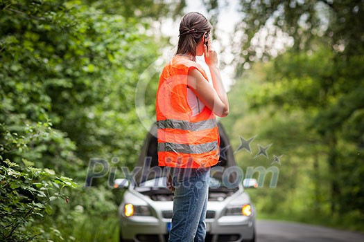 Young female driver wearing a high visibility vest, calling the roadside service/assistance after her car has broken down