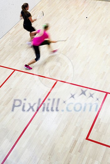 Two female squash players in fast action on a squash court (motion blurred image; color toned image) Two female squash players in fast action on a squash court (motion blurred image; color toned image)