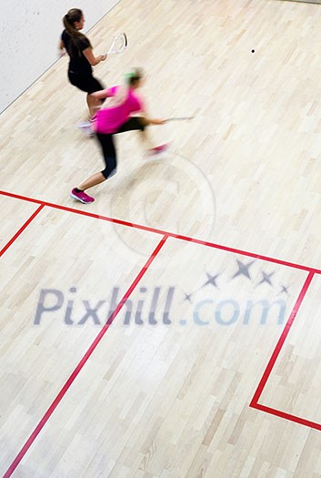 Two female squash players in fast action on a squash court (motion blurred image; color toned image)