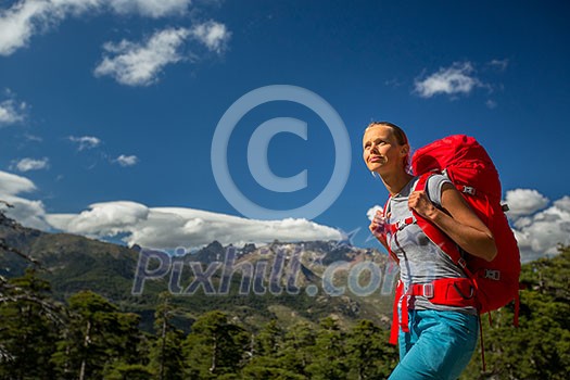 Pretty, female hiker in high mountains with her giant backpack, getting ready for some hiking