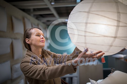 Pretty, young woman choosing the right lamp for her apartment in a modern home furnishings store (color toned image; shallow DOF)