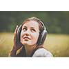 portrait of a pretty young woman listening to music on her mp3 player outdoors (daydreaming)