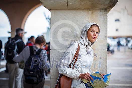 Gorgeous female tourist with a map discovering a foreign city - waiting for the rain to stop (shallow DOF; color toned image)