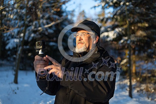 Handsome senior man shotting video with his adventura outdoor camera on a grip handle outdoors on a lovely winter day, enjoying retirement Handsome senior man shotting video with his adventura outdoor camera on a grip handle outdoors on a lovely winter day, enjoying retirement
