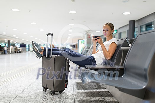 Young female passenger at the airport, using her tablet computer while waiting for her flight (color toned image)