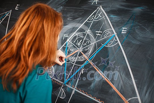 Portrait of a pretty young college student writing on the blackboard during a maths class (color toned image)