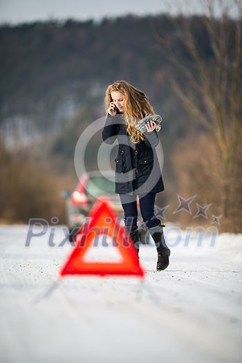 Young woman setting up a warning triangle and calling for assistance after her car broke down in the middle of nowhere on a freezing winter day Young woman setting up a warning triangle and calling for assistance after her car broke down in the middle of nowhere on a freezing winter day