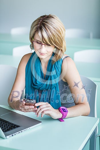 Pretty, young woman at an office, using a laptop and her smartphone