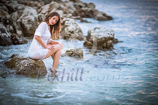 Attractive, young woman relaxing at the beach at sunset Attractive, young woman relaxing at the beach at sunset