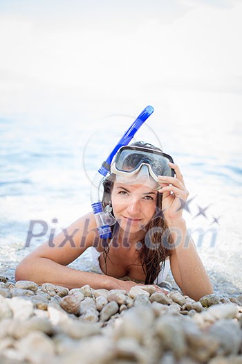 Pretty, young woman on a beach during her summer vacation with snorkel lying on beach with snorkeling mask and fins smiling happy enjoying the sun on a sunny summer day. Pretty, young woman on a beach during her summer vacation with snorkel lying on beach with snorkeling mask and fins smiling happy enjoying the sun on a sunny summer day.