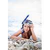 Pretty, young woman on a beach during her summer vacation with snorkel lying on beach with snorkeling mask and fins smiling happy enjoying the sun on a sunny summer day.