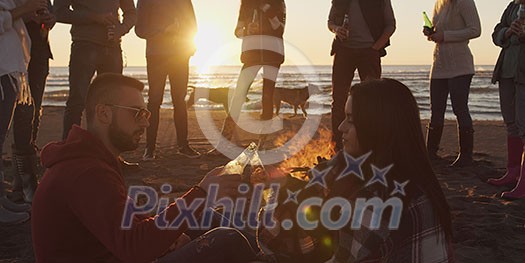 Happy Carefree Young Friends Having Fun And Drinking Beer By Bonefire On The Beach As The Sun Begins To Set Happy Carefree Young Friends Having Fun And Drinking Beer By Bonefire On The Beach As The Sun Begins To Set