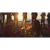 Happy Carefree Young Friends Having Fun And Drinking Beer By Bonefire On The Beach As The Sun Begins To Set