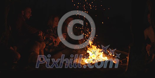 Young Couple Sitting with friends Around Campfire on The Beach At Night drinking beer