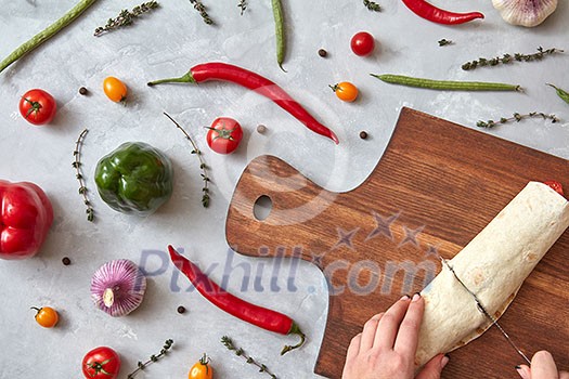 The girl cuts the finished burrito on a wooden board. Photo of a step-by-step cooking burrito. Top view, flat lay. The girl cuts the finished burrito on a wooden board. Photo of a step-by-step cooking burrito. Top view, flat lay.