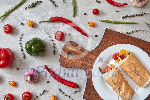 A tasty vegetable burrito on a plate on a wooden board, on a gray concrete background. Step-by-step recipe for cooking. Top view, flat lay. A tasty vegetable burrito on a plate on a wooden board, on a gray concrete background. Step-by-step recipe for cooking. Top view, flat lay.