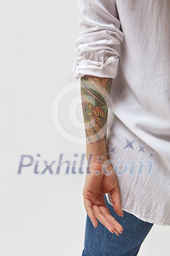 Back view of standing young woman with tattoo on hands. Isolated on gray background.