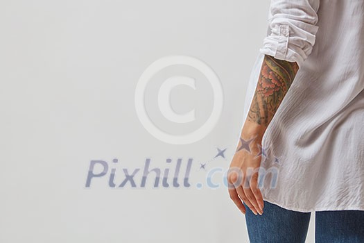 View from the back of a girl in jeans, a white shirt and with a tattoo on her hands on a gray background. Copy space