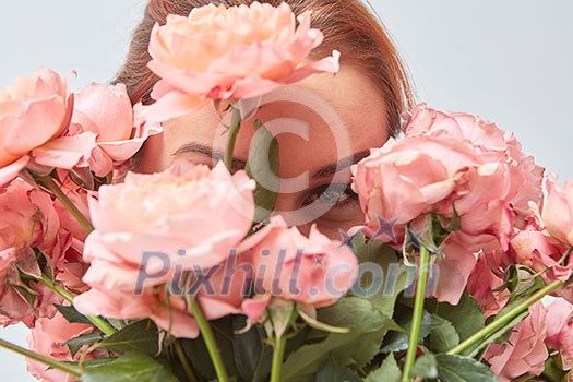A smiling woman hides her face behind a bouquet of fragrant pink roses. St. Valentine's Day. Women's Day. Close-up,