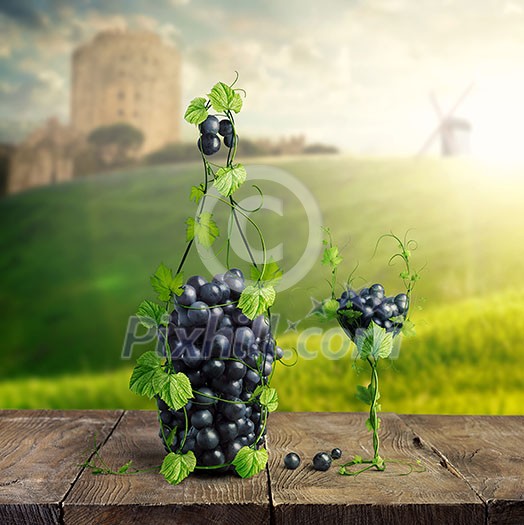 Bottle of Wine and a glass made by of grape leaves and a bunch of grapes on a wooden background with a blurred background view of the Castle, mill and the green lawn