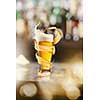 A cold glass of beer with beer foam and splash around on a wooden bar counter and blurred background with many bokeh