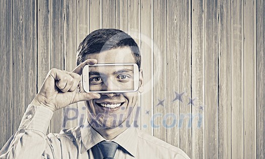 Young handsome businessman hiding mouth behind mobile phone