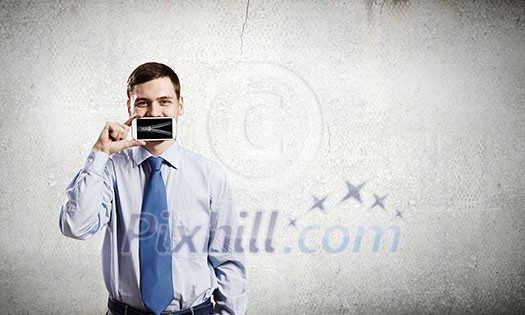 Young handsome businessman hiding mouth behind mobile phone