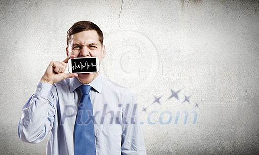 Young handsome businessman hiding mouth behind mobile phone