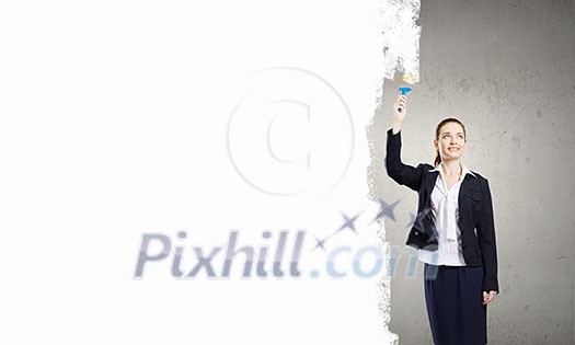 Young pretty businesswoman painting wall in white with brush