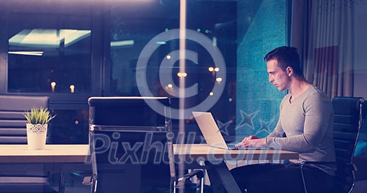 Young man working on laptop at night in dark office. The designer works in the later time.