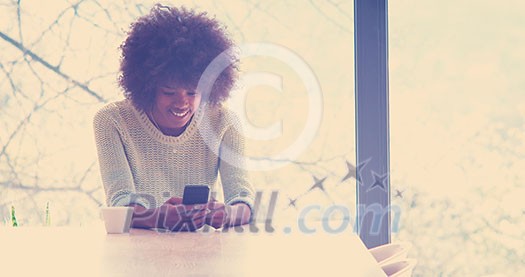 Handsome young african american woman drinking coffee and using a mobile phone at home Handsome young african american woman drinking coffee and using a mobile phone at home