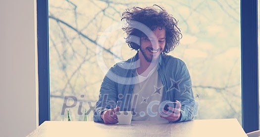 Handsome casual young man drinking coffee and using a mobile phone at home Handsome casual young man drinking coffee and using a mobile phone at home