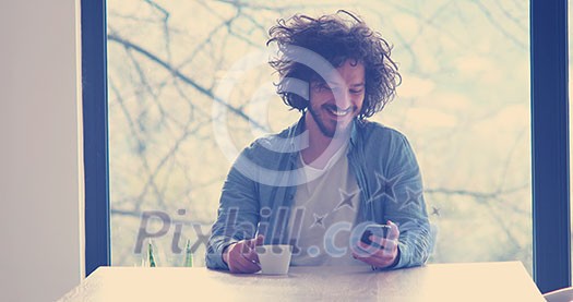 Handsome casual young man drinking coffee and using a mobile phone at  home