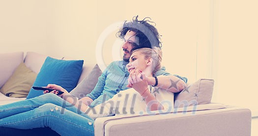 Young couple on the sofa watching television together in their luxury home